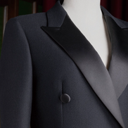 Close-up of women's black long overcoat with satin lapels and textured fabric, highlighting luxurious tailoring and sophisticated design.