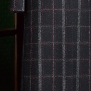 Close-up of bottom half of black plaid overcoat with red and white check pattern, showcasing double-breasted buttons and premium tailored finish.