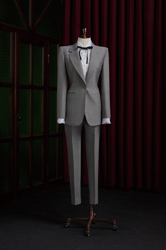 Women's tailored Black and White Pattern Suit, featuring structured shoulders, fitted waist, and white blouse with black ribbon, exuding vintage elegance.