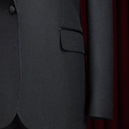 Close-up of women's black tuxedo suit with satin lapel, single-button closure, and flap pockets, showcasing luxurious tailoring and elegant design.