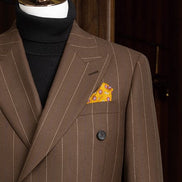 Close-up of a brown pinstripe men's suit jacket with double-breasted design, paired with a black turtleneck and accented by a vibrant orange pocket square for a refined, high-end look.
