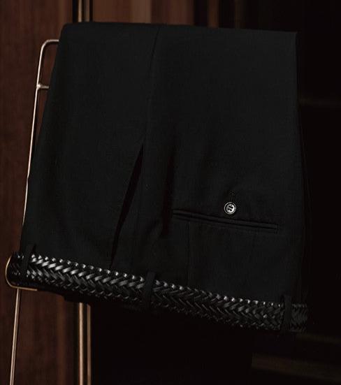 Close-up of black tailored trousers with intricate woven detailing on the hem, highlighting luxury craftsmanship and premium materials for a refined look.