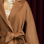 Close-up of a camel beige overcoat with elegant peak lapels and belted waist, showcasing luxurious wool fabric and refined tailoring for high-end style.