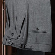 Close-up of grey tailored trousers by POLLHEIM, highlighting adjustable waist tabs and detailed stitching. Perfect for a refined, modern look with superior craftsmanship