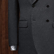 Close-up of a charcoal grey double-breasted suit, highlighting textured fabric, sleek buttons, and detailed sleeve finish with a patterned shirt cuff for added style.