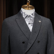 Close-up of a charcoal grey double-breasted suit on a mannequin, showcasing fine textured fabric, tailored lapels, and a decorative bee lapel pin for added elegance.