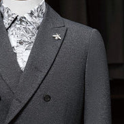 Close-up of a charcoal grey double-breasted suit, featuring refined lapels, a stylish bee lapel pin, and a contrasting patterned shirt, ideal for formal wear.