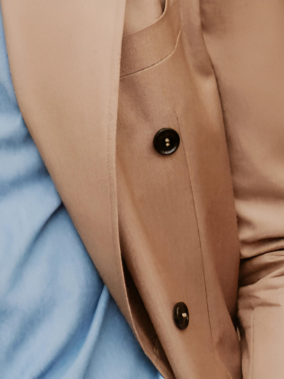Close-up of soft beige double-breasted suit buttons and pocket, highlighting refined tailoring and luxurious fabric, ideal for an elegant, formal look.