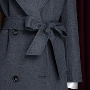 Close-up of a dark grey long overcoat with a waist tie belt, showcasing the premium wool fabric texture and double-breasted design, perfect for elegant layering.