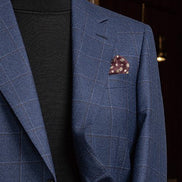Close-up of a deep blue check suit jacket pocket with a decorative pocket square, showcasing elegant tailoring.