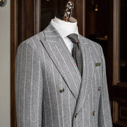 Close-up of a light grey double-breasted suit on a mannequin, showcasing fine textured fabric, tailored lapels, and green and orange detailed tie