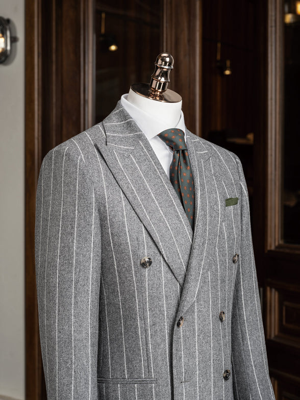 Close-up of a light grey double-breasted suit on a mannequin, showcasing fine textured fabric, tailored lapels, and green and orange detailed tie
