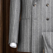 Close-up of a light grey double-breasted suit, highlighting textured lined fabric, sleek buttons, and detailed sleeve finish with a patterned shirt cuff for added style.