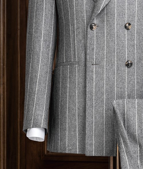 Close-up of a light grey double-breasted suit, highlighting textured lined fabric, sleek buttons, and detailed sleeve finish with a patterned shirt cuff for added style.