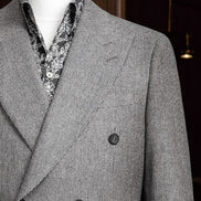 Close-up of a grey double-breasted suit on a mannequin, showcasing fine textured fabric, tailored lapels, and green and orange detailed tie
