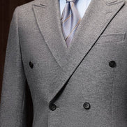 Close-up of a wool double-breasted suit on a mannequin, showcasing fine textured fabric, tailored lapels, and striped blue and gold tie