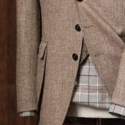 Elegant beige men's tweed blazer on a mannequin with a plaid shirt, floral tie, and pocket square, close up on buttons and pocket