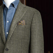 Detailed view of a green checked jacket with peak lapels and a decorative pocket square, epitomising sophisticated tailoring and craftsmanship