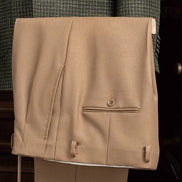 Close-up of beige tailored trousers, featuring a classic design with adjustable side tabs and a sleek pocket detail, paired with a green checked jacket.