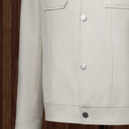 Close-up of The Couturist's white tailored jacket, highlighting snap button closure and front patch pockets. Luxurious women's tailored garment.