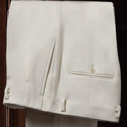 Close-up view of luxury white tailored trousers by The Couturist, showcasing double pleats and button detailing. High-end tailored pants for women