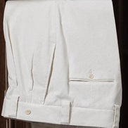 Close-up of cream-colored tailored trousers with cuffed hems and button details, showcasing refined craftsmanship and classic style
