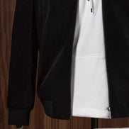 Stylish casual outfit featuring a black tailored zip-up jacket layered over a white hoodie and paired with cream-coloured trousers, displayed on a mannequin for modern streetwear style. Close-up on the zip and sleeves of the jacket 