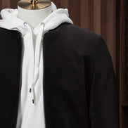 Stylish casual outfit featuring a black tailored zip-up jacket layered over a white hoodie and paired with cream-coloured trousers, displayed on a mannequin for modern streetwear style. Close up on the shoulder stitching 